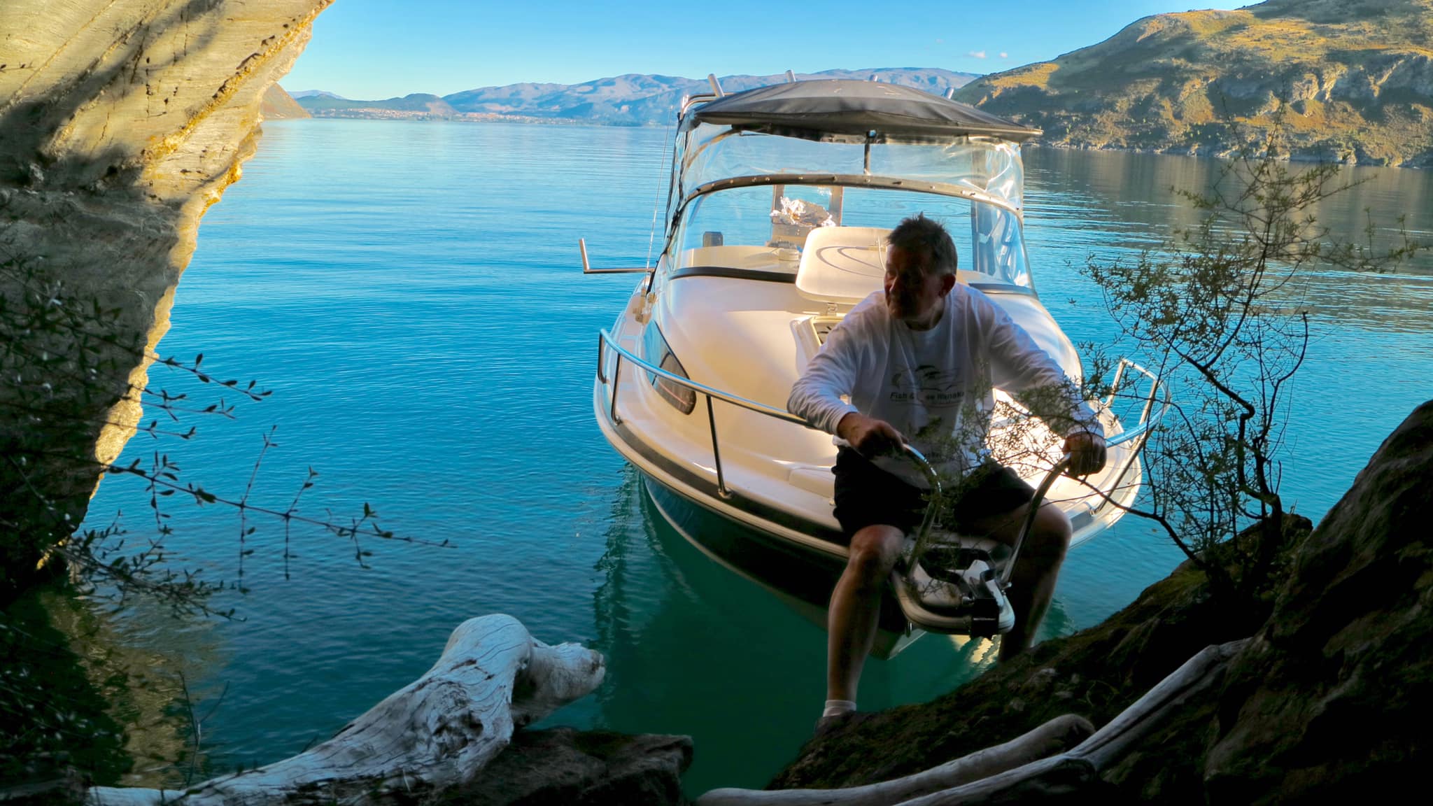 Skipper stepping off the boat onto the rocky shore of Lake Wanaka