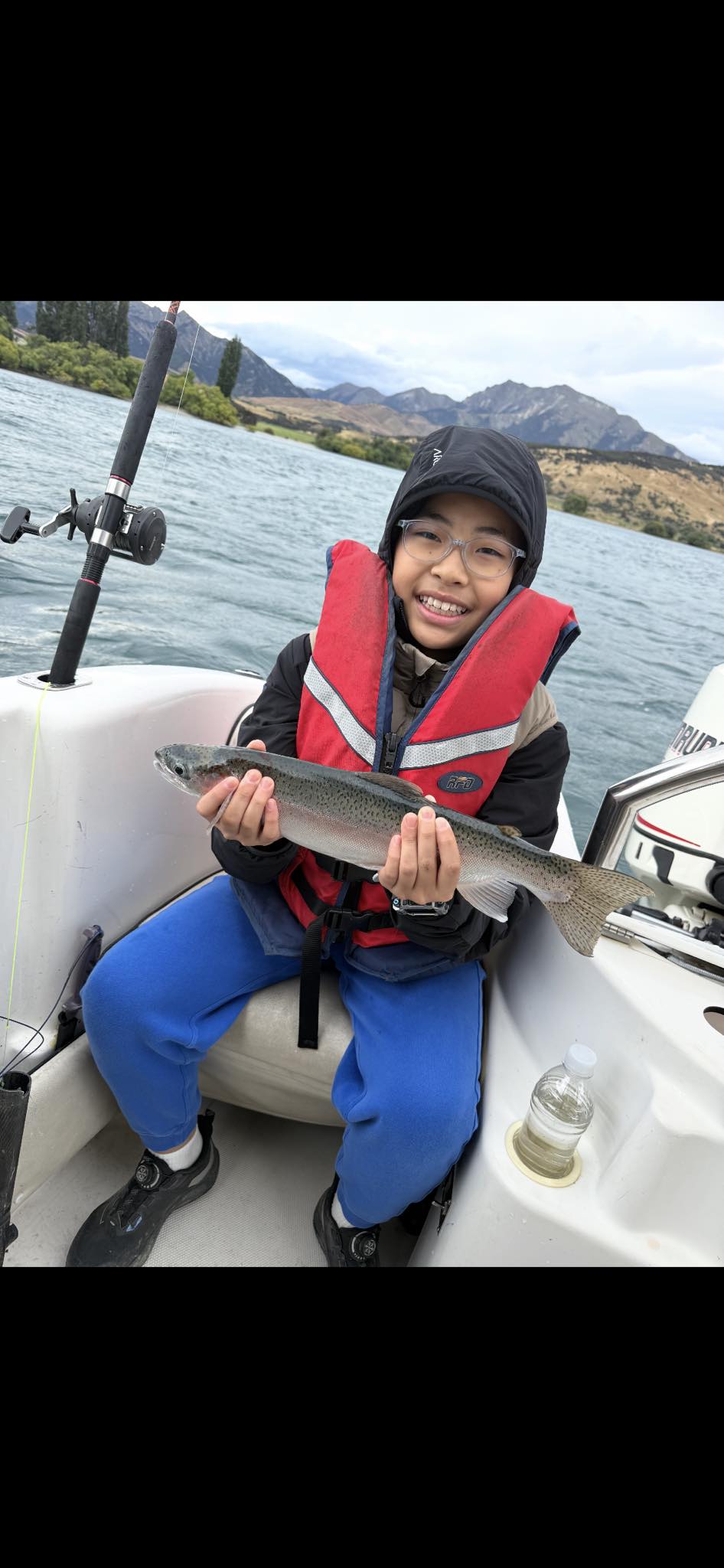 Young child in life jacket holding a fish on the boat